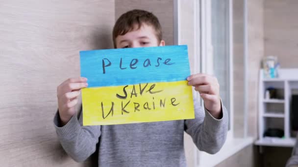 Niño sostiene una pancarta con una bandera azul y amarilla, Mensaje Por favor, salve Ucrania — Vídeos de Stock