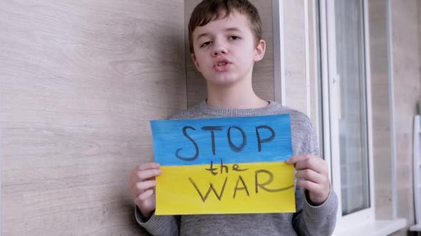 Niño sostiene en las manos un cartel con una bandera de Ucrania, y el mensaje Alto a la guerra — Vídeo de stock