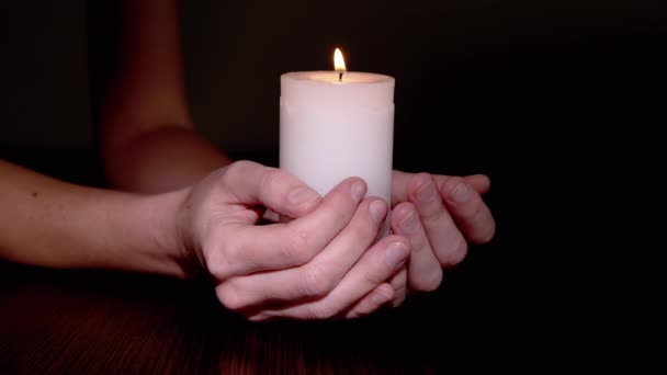 Женщина держит белую восковую свечу, жгущую на столе в темной комнате. — стоковое видео