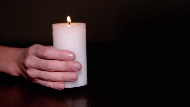 Female Hand zet een brandende witte kaars op tafel in een donkere kamer. Sluiten. — Stockvideo