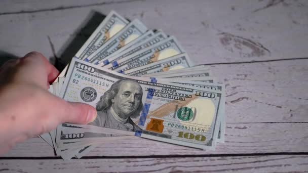 Женщина берет стопку раздутых банкнот по 100 долларов, лежащих на столе — стоковое видео