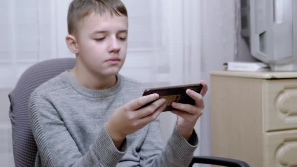 Kind sitzt auf Stuhl, hält Smartphone in den Händen, liest SMS auf Bildschirm — Stockvideo