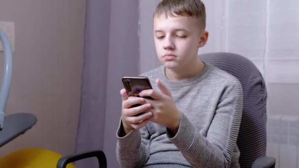 Το παιδί κάθεται σε μια καρέκλα, κρατά ένα Smartphone in Hands, γράφει SMS in Chat. Κλείσε. — Αρχείο Βίντεο