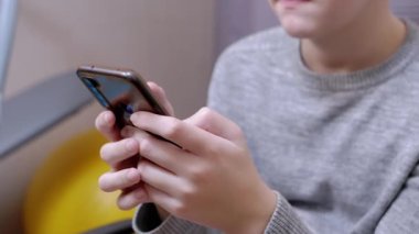 Çocuk bir sandalyede oturur, elinde akıllı telefon tutar, yatak odasında oynar. Kapat.