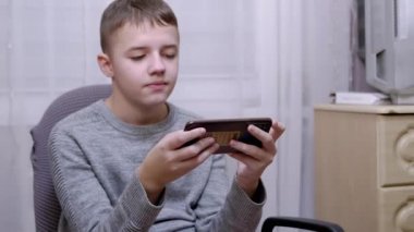 Çocuk bir sandalyede oturur, elinde bir akıllı telefon tutar, ekranda SMS okur