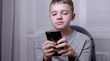 Çocuk bir sandalyede oturur, elinde akıllı telefon tutar, yatak odasında oynar. Kapat.