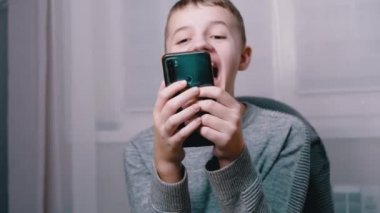 Gergin bir şekilde gülen duygusal çocuk akıllı telefon ekranına parmağını soktu. 4K