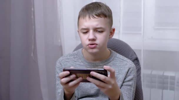 Ребенок сидит в кресле, держит смартфон в руках, читает SMS на экране. 4K — стоковое видео