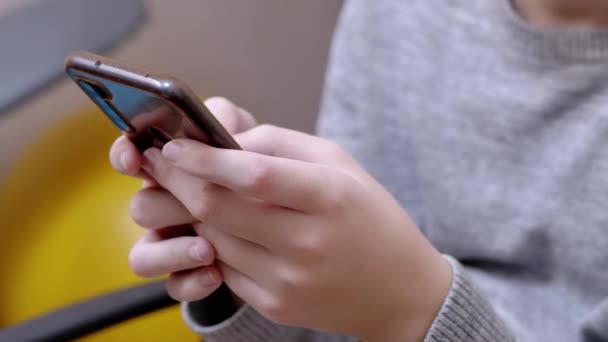 Criança senta-se em uma cadeira, segura um smartphone em mãos, joga no quarto. Fechar — Vídeo de Stock