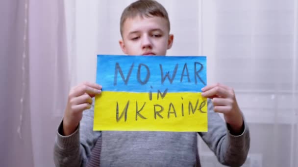 Дитина тримає в руках прапор з прапором України і повідомлення "Без війни" — стокове відео