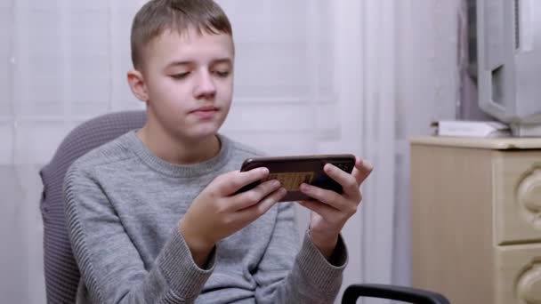 Dziecko siedzi na krześle, trzyma smartfon w rękach, czyta SMS-y na ekranie — Wideo stockowe