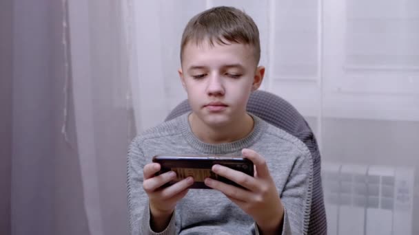 Ребенок сидит в кресле, держит смартфон в руках, читает SMS на экране. 4K — стоковое видео