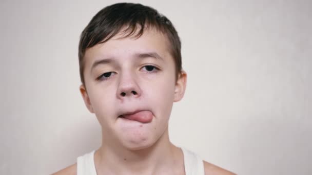Egy fiú leeresztett szemmel nyalogatja a száját a nyelvével, a kamerába néz. — Stock videók