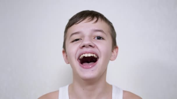 Pojken skrattar medan du tittar på kameran, hans mun vidöppen, visar sina tänder — Stockvideo