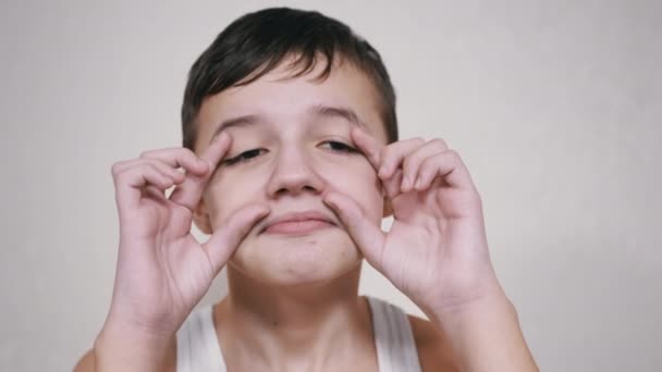 Positief kind raakt zijn gezicht met zijn handen, Grimaces, kijken naar de camera — Stockvideo