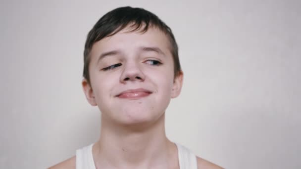Um menino sorridente com pálpebras abaixadas gira seus olhos em direções diferentes. 4K — Vídeo de Stock