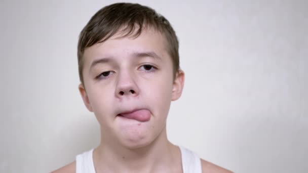 A Boy with a Lowered Eyelid Licks his Lips with his Tongue, Looks at the Camera — Stock Video