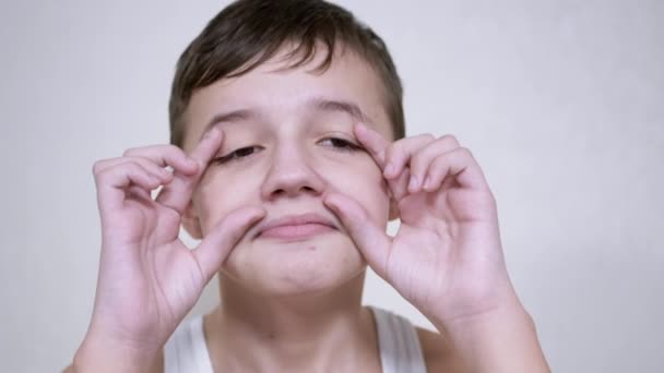 Criança positiva toca seu rosto com as mãos, Grimaces, olhando para a câmera — Vídeo de Stock