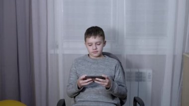 Gülümseyen Çocuk Bir Sandalyede Oturup Odada Bir Akıllı Telefondan Konuşuyor. 4K