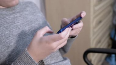 Çocuk bir sandalyede oturur, elinde akıllı telefon tutar, yatak odasında oynar. Kapat.