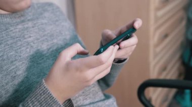 Çocuk bir sandalyede oturur, elinde akıllı telefon tutar, yatak odasında oynar. Kapat.