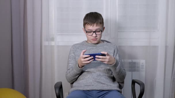 Умный мальчик в очках смотрит видео в мобильном приложении по телевизору. — стоковое видео