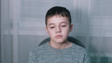 Üzgün Suçlu Çocuk, bir odada tek başına bir koltukta oturuyor ve aşağıya bakıyor.