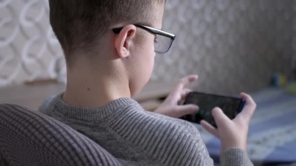 Time Lapse Child en gafas se sienta en una silla, juega videojuegos en un teléfono inteligente — Vídeos de Stock