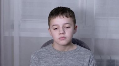 Üzgün Suçlu Çocuk, bir odada tek başına bir koltukta oturuyor ve aşağıya bakıyor.
