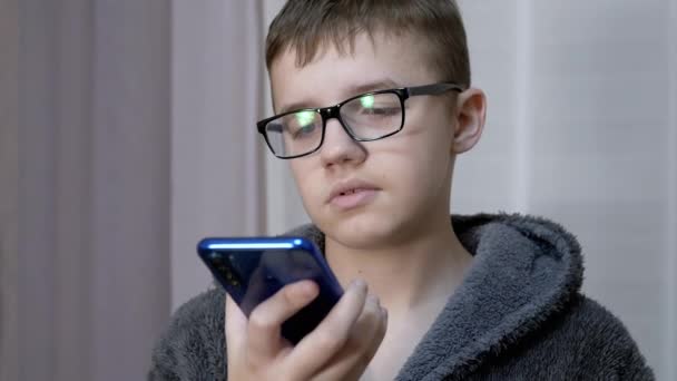 Smutne dziecko w okularach trzyma smartfon w rękach, rozmawia przez łącze wideo w pokoju — Wideo stockowe