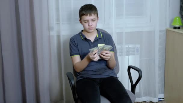 Seriózní teenager počítání stohu 100 dolarů účty zatímco sedí v křesle — Stock video