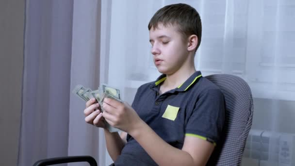 Seriózní teenager počítání stohu 100 dolarů účty zatímco sedí v křesle — Stock video