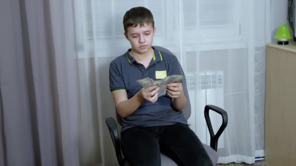 Grave adolescente contare una pila di bollette da 100 dollari mentre seduto su una sedia — Video Stock