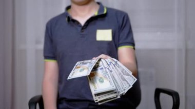Zengin çocuk elinde 100 dolarlık banknotlar tutuyor ve sallıyor.