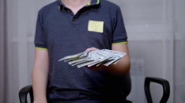 Zengin çocuk elinde 100 dolarlık banknotlar tutuyor ve sallıyor.