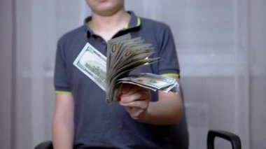Zengin çocuk elinde 100 dolarlık banknotlar tutuyor ve sallıyor.