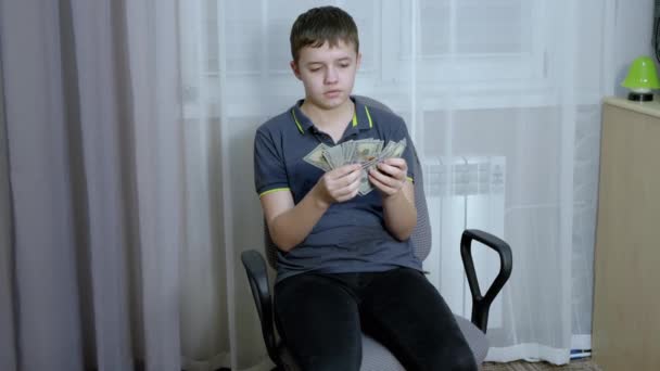 Adolescente sério contando uma pilha de contas de 100 dólares enquanto sentado em uma cadeira — Vídeo de Stock