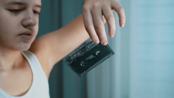 Παιδί κρατά ένα παλιό μαύρο Vintage Audio Cassette στα χέρια του, το εξετάζει. 4K — Αρχείο Βίντεο