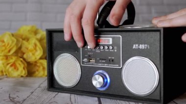 Taşınabilir bir ses kayıt cihazında Kadın Eller Tuşlara Basıyor. Ses, oyun, önceki, mod. Oyuncu, masadaki çiçeklerin arka planına USB girdisi olan iki stereo hoparlörlü radyo.
