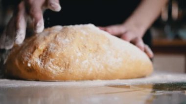 Dişi Eller Maya Hamuru 'nu diz çöktürüp masaya un serpiyor. Ekmek ve çörek yapmak için sarı, pürüzsüz hamur. Evdeki aile için lezzetli hamur işleri hazırlıyorum. Yavaş çekim.