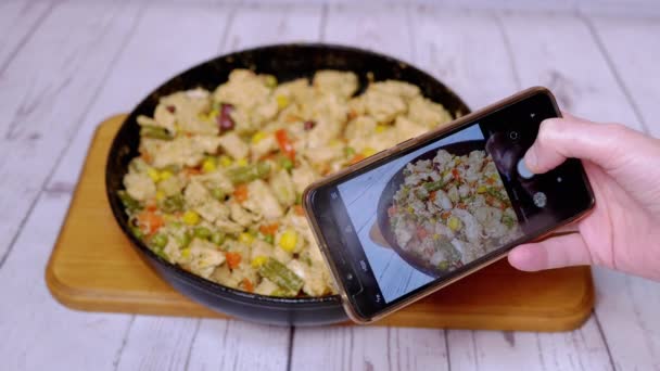 女性在智能手机相机上拍摄带有蔬菜的油炸肉 一个煎锅的特写与多汁炖鸡肉片 与五彩斑斓的蔬菜混合 家庭厨房 — 图库视频影像