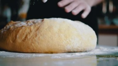 Dişi Eller Maya Hamuru 'nu diz çöktürüp masaya un serpiyor. Ekmek ve çörek yapmak için sarı, pürüzsüz hamur. Evdeki aile için lezzetli hamur işleri hazırlıyorum. Yavaş çekim.