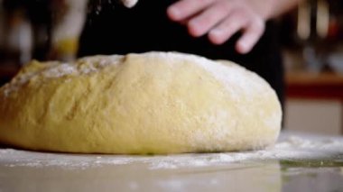 Dişi Eller Maya Hamuru 'nu diz çöktürüp masaya un serpiyor. Ekmek ve çörek yapmak için sarı, pürüzsüz hamur. Evdeki aile için lezzetli hamur işleri hazırlıyorum. Yavaş çekim.