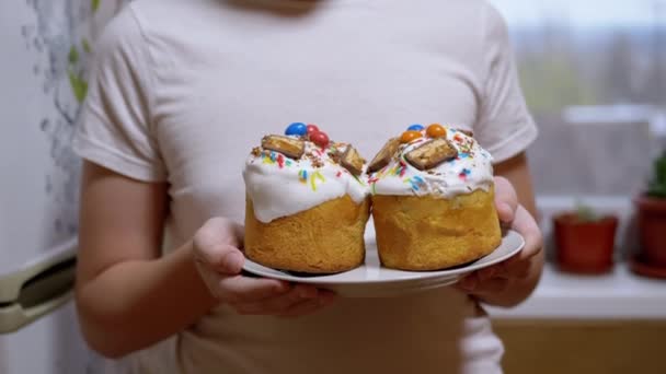小孩在盘子里抱着两只复活节的蛋糕 站在厨房里 美味的复活节纸杯蛋糕用白色糖霜和五颜六色的五彩纸屑装饰 东正教复活节 — 图库视频影像