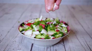 Sebze salatasına turp, salatalık, yeşillik serpiştirilmiş Eller Şefi Salatası. Yavaş çekim. Renkli yeşil soğan, maydanoz, turp ve salatalık sebzesi karışımı, yağ. Vejetaryen diyeti. Sağlıklı yemek..