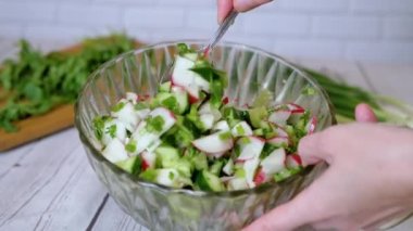 Sebze salatası, salatalık, salatalık, yeşillik ve sebzeyle karıştırılan eller. Yakın plan. Renkli yeşil soğan, maydanoz, turp ve salatalık sebzesi karışımı, yağ. Vejetaryen diyeti. Sağlıklı yemek..