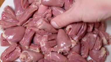 Dişi El, taze çiğ tavuk kalplerini tabağa koydu. Yakın plan. Bir sürü parlak kırmızı tavuk kalbi var, ikiye bölünmüş. Beslenme eti. İkinci sınıfın yan ürünleri. Fakirler için ucuz yemek..