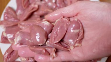 Dişi El, taze çiğ tavuk kalplerini tabağa koydu. Offal. Bir sürü parlak kırmızı tavuk kalbi var, ikiye bölünmüş. Beslenme eti. İkinci sınıfın yan ürünleri. Fakirler için ucuz yemek..