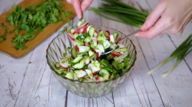 Sebze salatası, salatalık, salatalık, yeşillik ve sebzeyle karıştırılan eller. Yakın plan. Renkli yeşil soğan, maydanoz, turp ve salatalık sebzesi karışımı, yağ. Vejetaryen diyeti. Sağlıklı yemek..