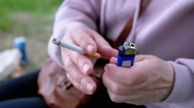 Elinde sigara tutan kadın ve doğada güneşin altında oturan bir çakmak. Dışarıda sigara içen bir kadın, park eder. Sigara içiyorum. Kötü alışkanlık. Bağımlılık. Sağlıksız yaşam tarzları. Stres yüzünden. Dinleniyor.